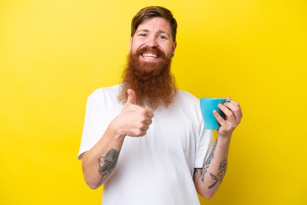 Homem ruivo com barba segurando uma caneca isolada em fundo amarelo com polegares para cima porque algo bom aconteceu