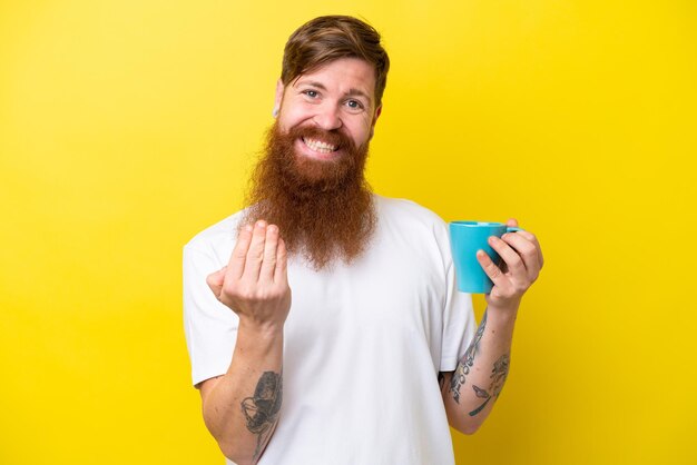 Homem ruivo com barba segurando uma caneca isolada em fundo amarelo convidando para vir com a mão Feliz por você ter vindo