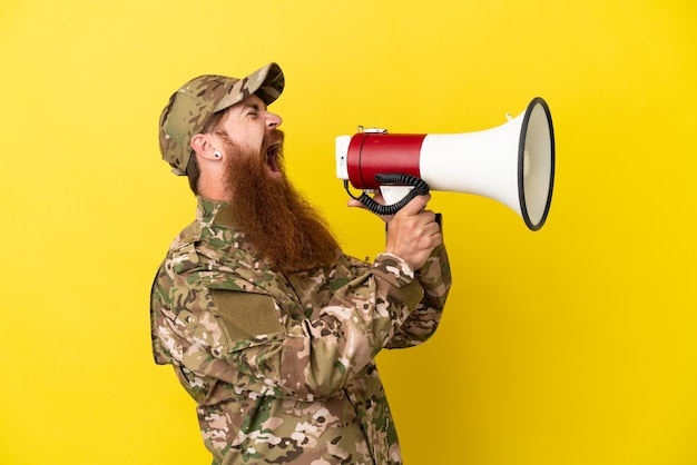 Homem ruivo militar isolado em um fundo amarelo gritando em um megafone