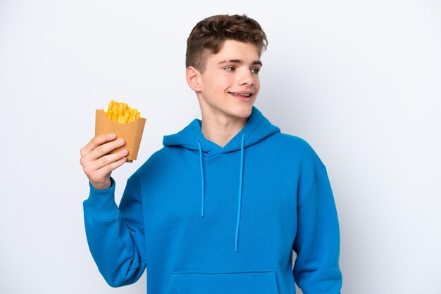 Homem russo adolescente segurando batatas fritas isoladas em fundo branco pensando em uma ideia enquanto olha para cima