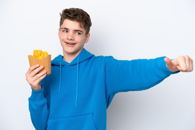 Homem russo adolescente segurando batatas fritas isoladas no fundo branco, dando um polegar para cima gesto