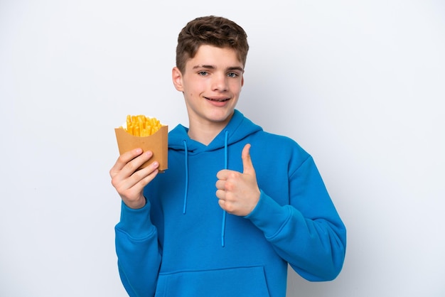Homem russo adolescente segurando batatas fritas isoladas no fundo branco, dando um polegar para cima gesto