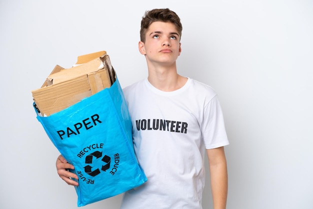 Homem russo adolescente segurando um saco de reciclagem cheio de papel para reciclar isolado no fundo branco e olhando para cima