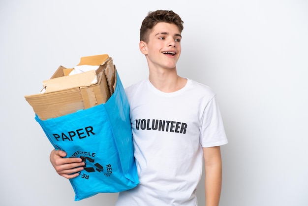 Homem russo adolescente segurando um saco de reciclagem cheio de papel para reciclar isolado no fundo branco rindo