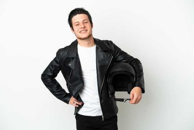 Homem russo com capacete de motociclista isolado no fundo branco, posando com os braços na cintura e sorrindo