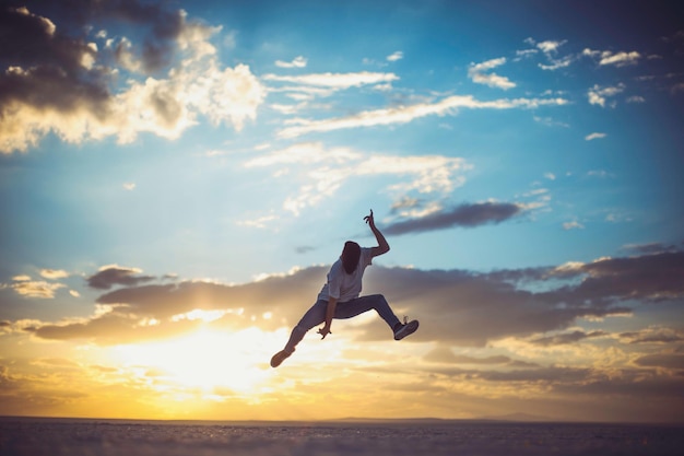 Homem saltando sobre o sal contra o céu durante o pôr do sol