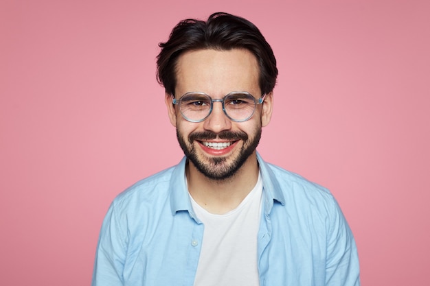 Homem satisfeito com óculos e sorrisos isolados sobre rosa