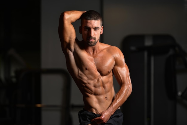 Homem saudável em pé forte na academia e flexionando os músculos muscular atlético fisiculturista modelo de fitness posando após exercícios