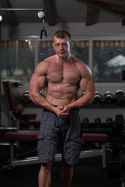 Homem saudável em pé forte na academia e flexionando os músculos Muscular Atlético Fisiculturista Modelo de fitness posando após exercícios