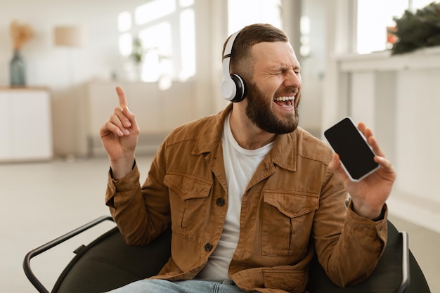 Homem se divertindo cantando segurando smartphone ouvindo música em casa