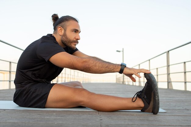 Foto homem se estende alcançando seus dedos dos pés durante o treino de fitness ao ar livre