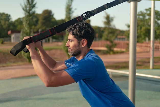 Homem se exercitando ao ar livre no parque ensolarado Ótimo treino de TRX e se exercitando ao ar livre