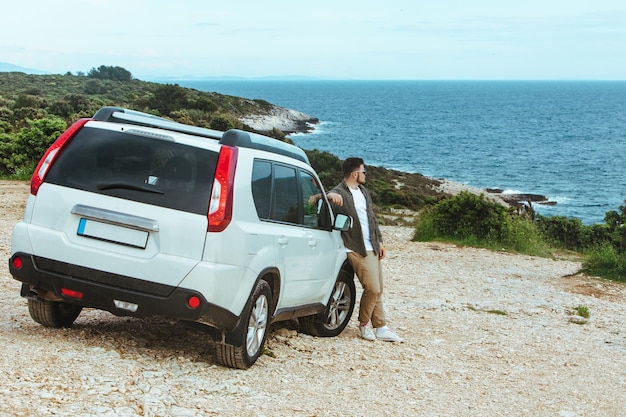 Homem se inclina no carro suv apreciando a vista do conceito de estilo de vida de férias de viagem de verão no mar