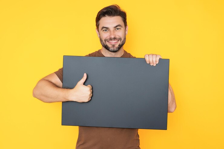 Foto homem segura cartaz cartão em branco placard pronto para promoção e venda espaço para sinal e texto homem mostrando o polegar para cima homem com cartaz em branco no fundo do estúdio homem com o pulgar para cima segura o quadro em branco
