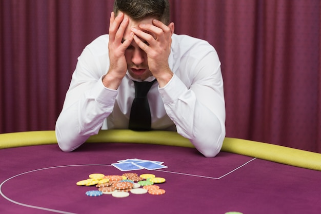 Homem segurando a cabeça nas mãos na mesa de poker