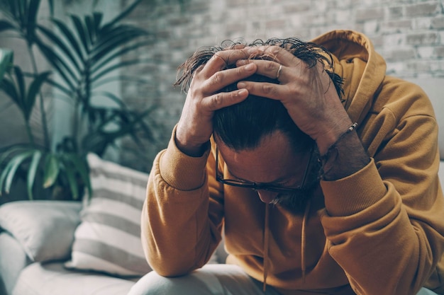 Homem segurando a cabeça sozinho em casa para emoções de desespero e estresse conceito de adulto cansado e crise pessoal tristeza e retrato estressado do interior masculino tendo problemas e preocupado más notícias