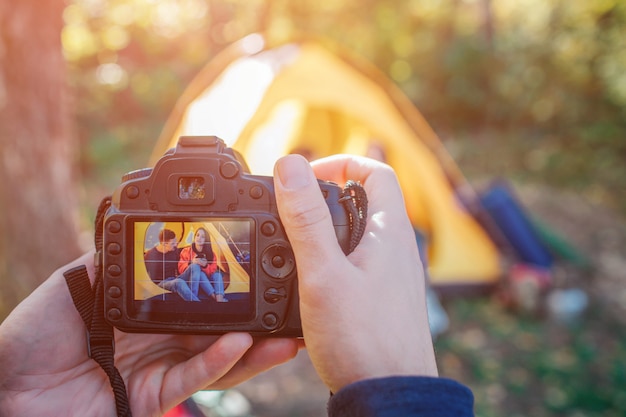 Homem segurando a câmera que tira foto do casal. eles se sentam na tenda.