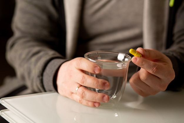 Homem segurando a cápsula multivitamínica e um copo de água. foto de close