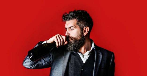 Homem segurando a garrafa com champanhe, vinho. A pessoa segura uma garrafa de vinho tinto na mão. Homem barbudo com uma garrafa de champanhe e uma taça. Homem elegante em smoking, terno, jaqueta.