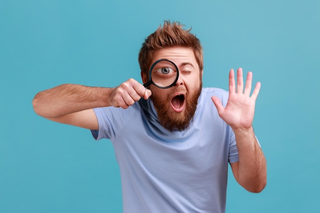 Homem segurando a lupa e olhando para a câmera com grande zoom olho acenando a mão dizendo oi