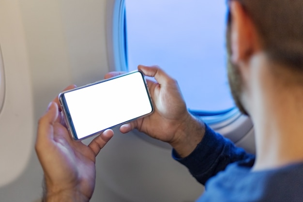 Homem segurando a tela em branco mockup smartphone nas mãos no avião.