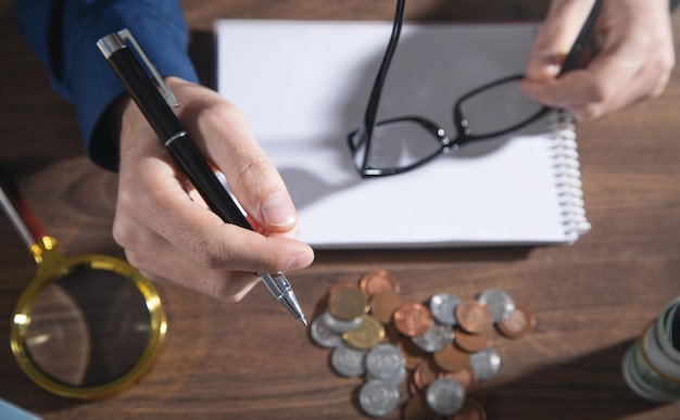 Homem segurando caneta com uma contagem de moedas na mesa