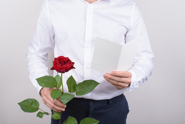 Homem segurando cartão postal e rosa isolado fundo cinza