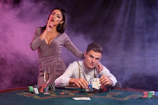 Homem segurando cartas jogando pôquer no cassino sentado à mesa com pilhas de fichas celebra vitória