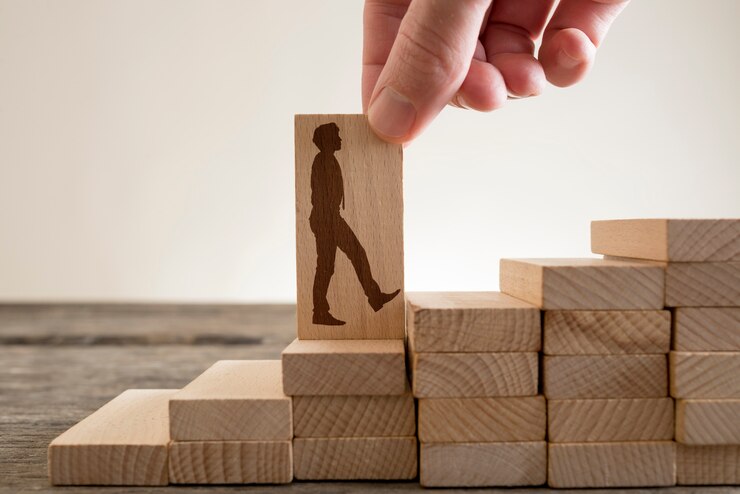 Foto homem segurando com os dedos o dominó de madeira com forma de empresário subindo escadas para subir a escada da carreira.