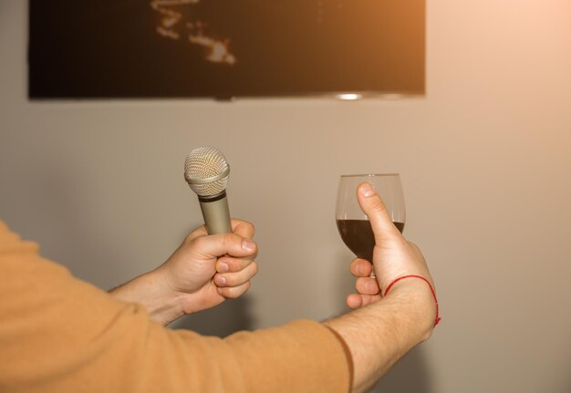 Homem segurando copos de vinho e microfone. Festa noturna, divirta-se, cantando no karaokê.