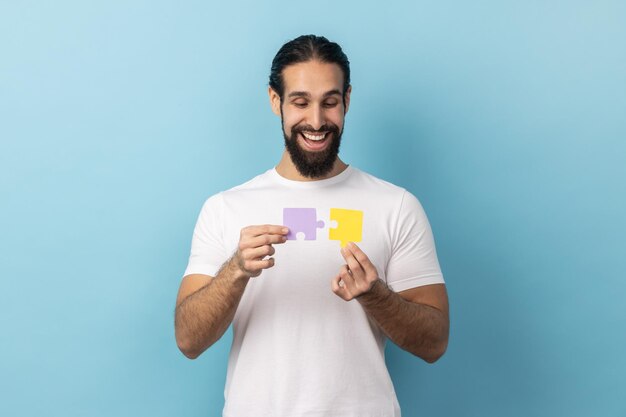 Foto homem segurando duas peças de quebra-cabeça e sorrindo alegremente pronto para conectar peças de quebra-cabeça símbolo de união