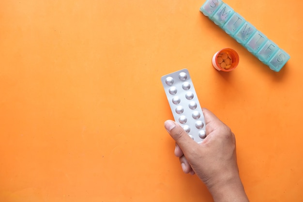 Homem segurando embalagens blister com o recipiente do medicamento e a caixa de comprimidos na mesa