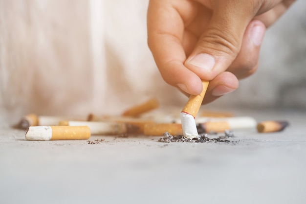 Homem segurando fumando um cigarro na mão escura.