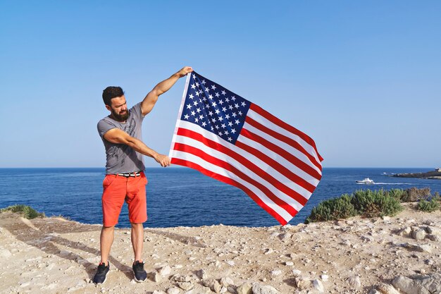 Homem segurando grande acenando a bandeira dos eua ao ar livre. dia da independência dos estados unidos da américa. conceito de povo patriótico americano