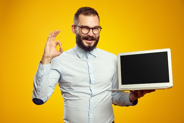 Homem segurando laptop e mostrando uma tela em branco enquanto mostra o sinal de aprovação