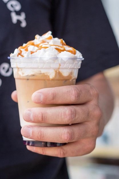 Homem segurando latte frio com chantilly Latte gelado decorado com cobertura de caramelo salgado na mão