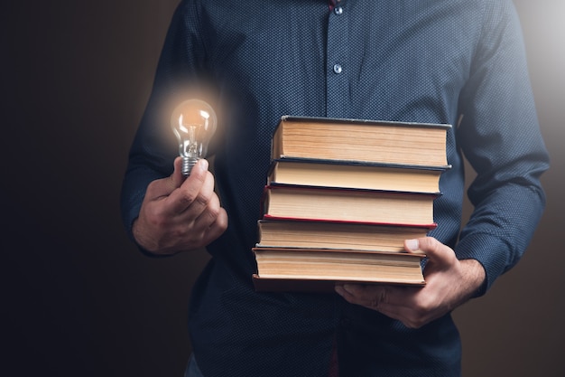 Homem segurando livros e uma lâmpada. ideias conceituais de livros