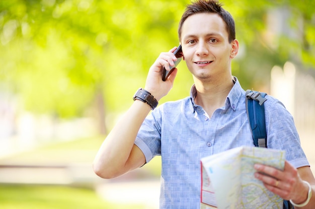 Homem segurando mapa ao ar livre e falando ao telefone