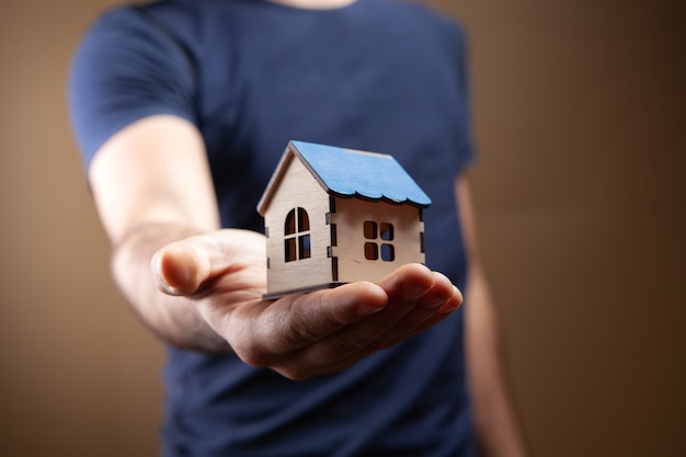 Homem segurando modelo de casa em fundo marrom