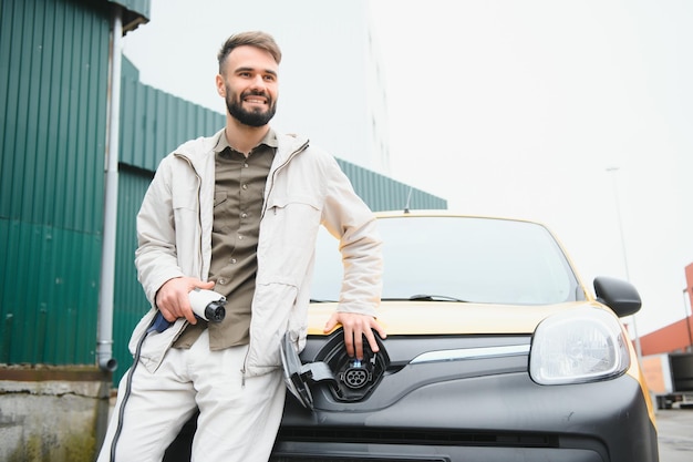 Homem segurando o cabo de carregamento de energia para carro elétrico no estacionamento ao ar livre e ele vai conectar o carro à estação de carregamento no estacionamento perto do shopping