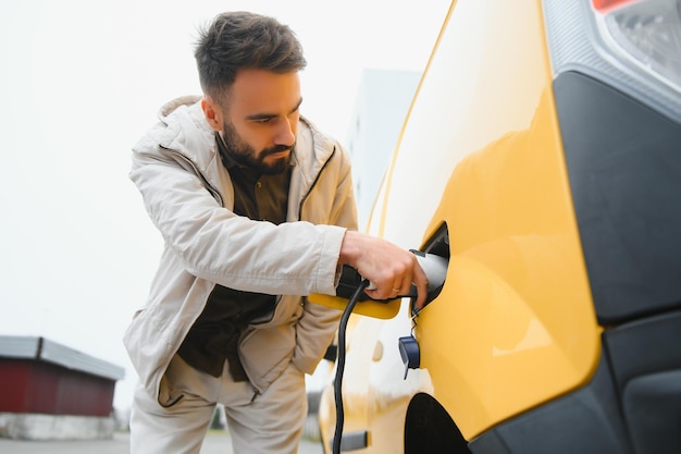 Homem segurando o cabo de carregamento de energia para carro elétrico no estacionamento ao ar livre e ele vai conectar o carro à estação de carregamento no estacionamento perto do shopping