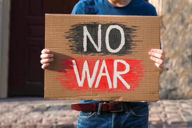 Homem segurando o cartaz com as palavras Sem guerra na rua da cidade closeup
