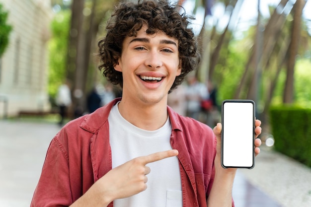 Homem segurando o telefone com tela em branco na mão mostrando para a câmera e apontando para o dispositivo