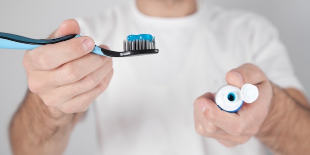 Homem segurando pasta de dente azul e escova de dente