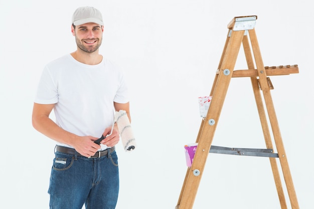 Homem segurando rolo de pintura enquanto está de pé por uma escada