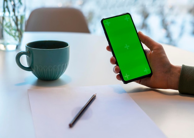 Homem Segurando Smartphone com Chroma Key Screen no lápis de mesa branco na tela de papel verde mock up