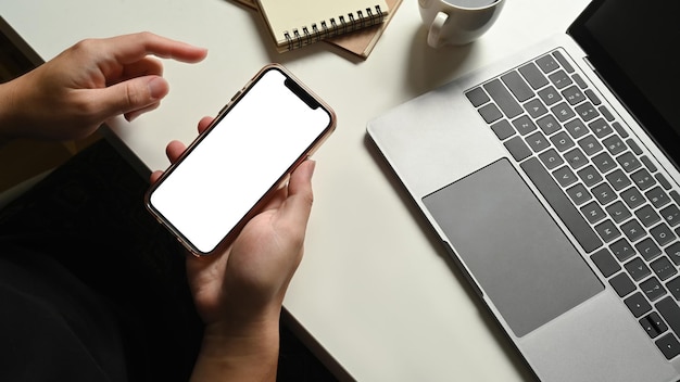 Homem segurando smartphone com tela vazia no espaço de trabalho com vista superior