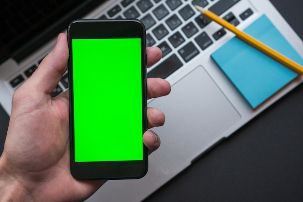 Homem segurando Smartphone com tela verde Chroma Key no fundo, local de trabalho moderno
