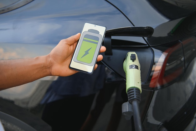 Homem segurando smartphone enquanto carrega carro na estação de carregamento de veículos elétricos closeup