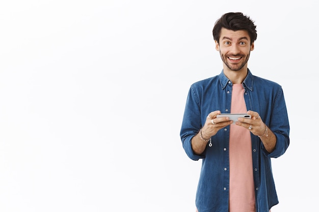 homem segurando smartphone horizontalmente e olhar a câmera encantado, venceu no jogo, bateu pontuação e triunfou